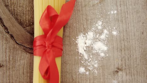 Bunch-of-raw-spaghetti-tied-up-with-red-ribbon-on-wooden-background-sprinkled-with-floor