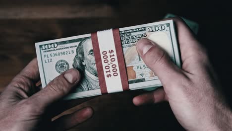 una pila de billetes de 10.000 dólares estadounidenses en manos masculinas sobre un fondo de madera.