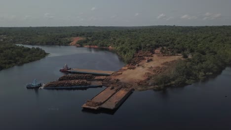 climate change and deforestation: loading logs from the amazon rainforest on barges for transport - aerial flyover