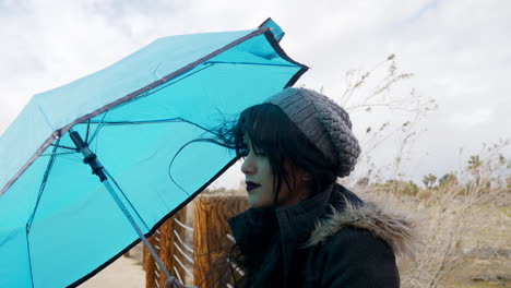 una mujer atractiva con un paraguas azul con mal tiempo mientras el viento sopla en una tormenta de lluvia bajo cielos nublados