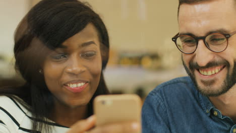 Close-up view of young caucasian man using smartphone and showing a video to african american woman a in a coffee shop