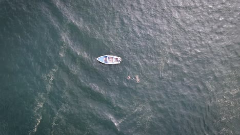 ascending drone shot of a fishing boat in the ocean with people swimming