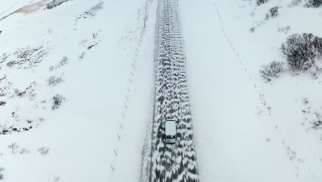 Aerial-Tracking-Tilt-Reveal-View-of-Van-Car-Driving-Moving-on-a-Snowy-Road-in-Winter-Through-Wild-Area-and-Vast-White-Snow-Covered-Lands-in-Mount-Búlandstindur-Region,-Iceland