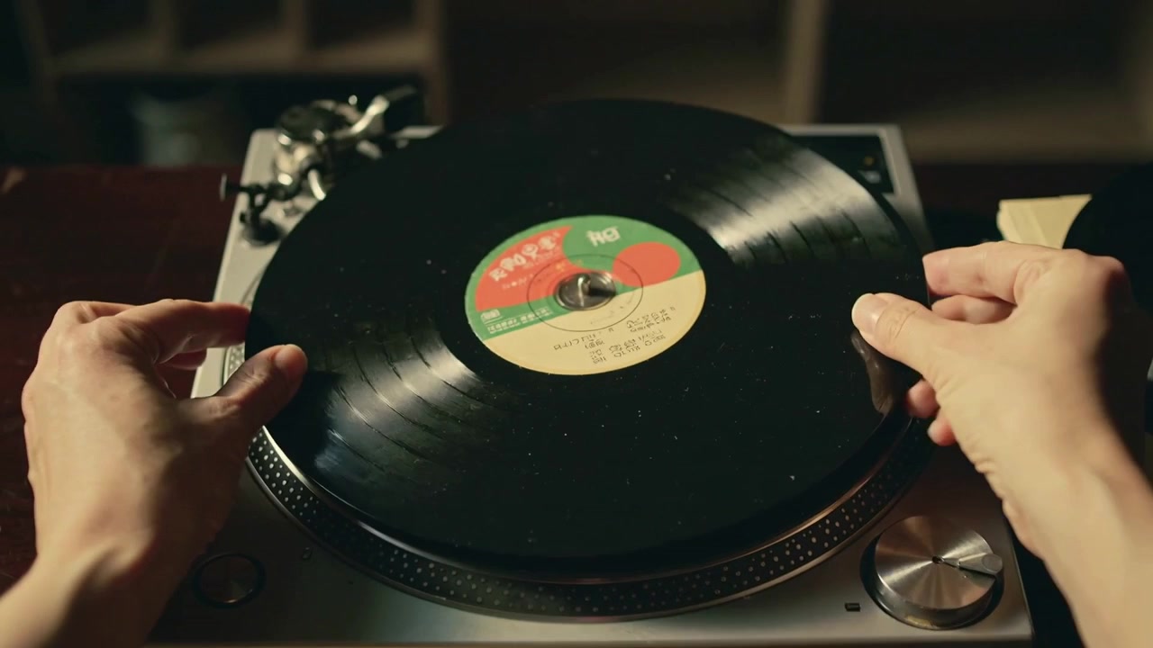 Mani maschili che si allungano per sollevare e centrare un vinile su un giradischi a casa per la riproduzione, con una pila di dischi.