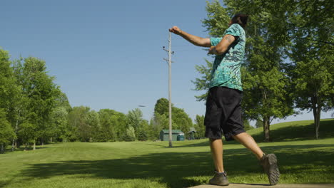 een man voert een krachtige drive uit in een disc golf spel, het tentoonstellen van zijn atletische vorm en techniek tegen een achtergrond van heldere blauwe hemel en weelderig groen