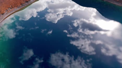las aguas turquesas del lago lavodilec con nubes que se reflejan, terreno montañoso, vista aérea