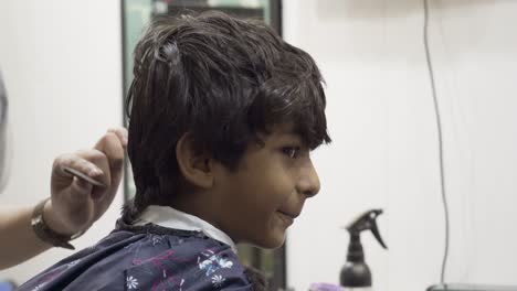 a young asian boy in a salon is smiling at the camera while getting his hair trimmed.