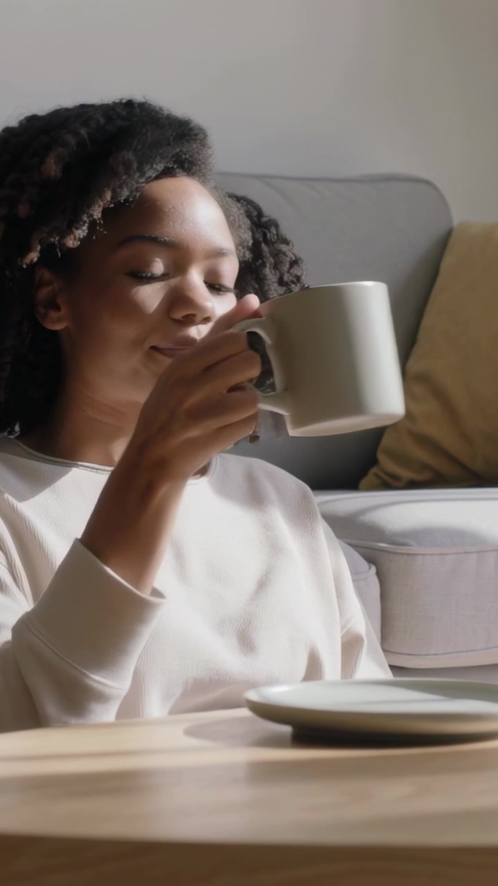 Vertical video: Lifting woman in light top sipping mug at home, relaxing, placing mug on saucer
