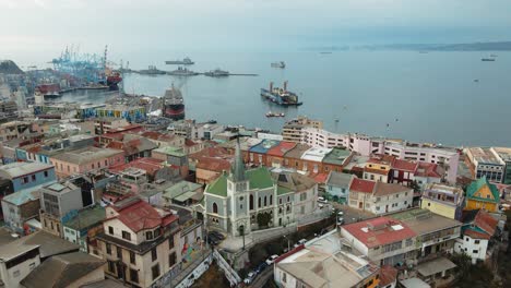 aerial dolly in of colorful houses and lutheran church leading to valparaiso sea port and ships docked, chile