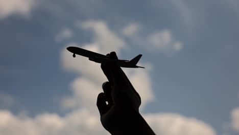 silhouette of a hand holding a toy airplane against a cloudy sky
