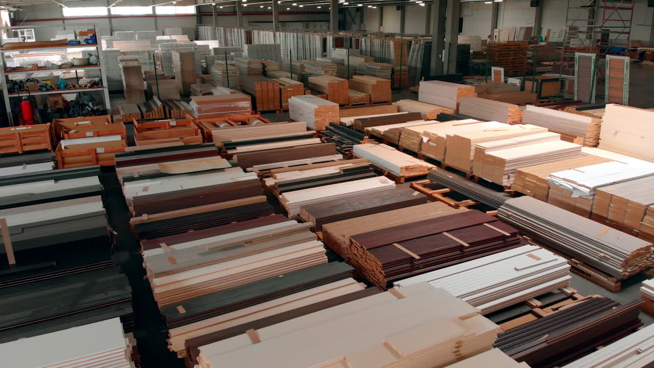 Wooden planks of diverse colors stored in the large premises. Piles of timber materials for door manufacturing.