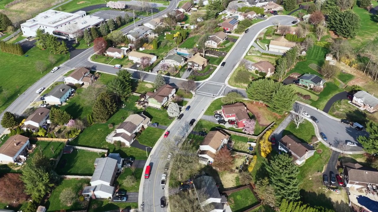 Sorvolo aereo di un tranquillo quartiere suburbano ad Akron, Pennsylvania, con strade residenziali curve, case tradizionali, prati verdi primaverili, alberi e una tranquilla comunità di piccola città in una giornata di sole