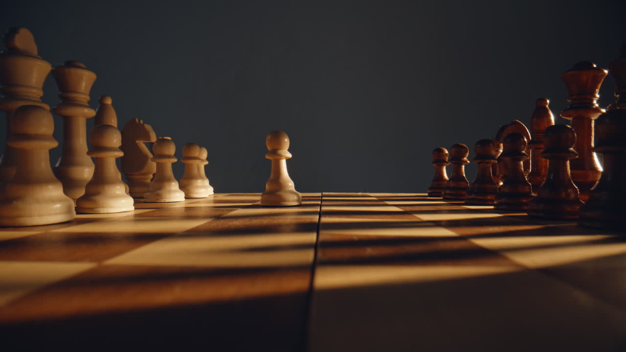 Hand first chess move at chessboard indoor closeup. Unknown player moving pawn