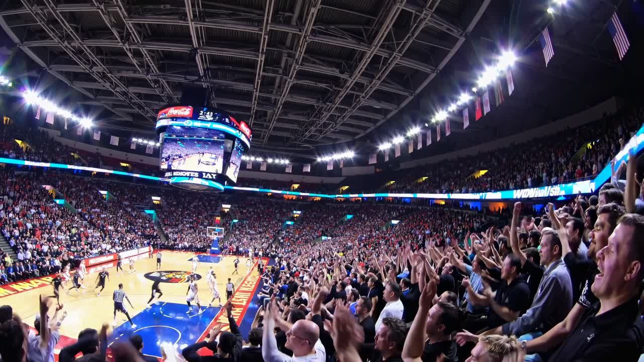 Enthousiaste menigte juicht bij een professionele basketbalwedstrijd in een grote arena.