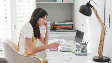 biracial woman in headphones having laptop video call sitting at desk working at home, slow motion