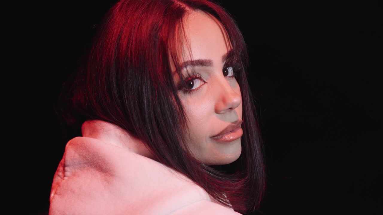 Young beautiful woman with white sweater. in the night looking into the camera, dark surroundings, posing in slow motion, filmed from the side, close up