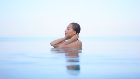 a young, attractive woman pushes back her wet hair as she enjoys the swimming pool