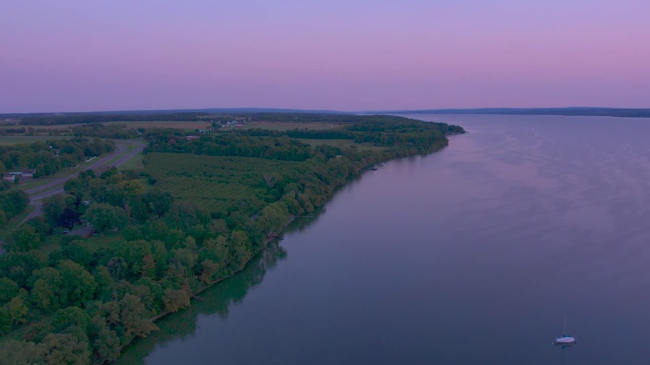 красивый полет беспилотника над берегами озера сенека, деревьями и лодками нью-йорка в лучах багрового заката