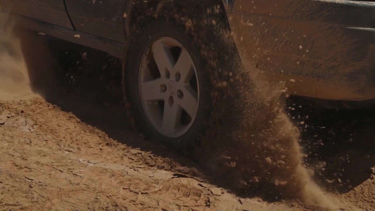 Dirty off road SUV tire spinning through sandy desert ground throwing up sand grains in southern Morocco