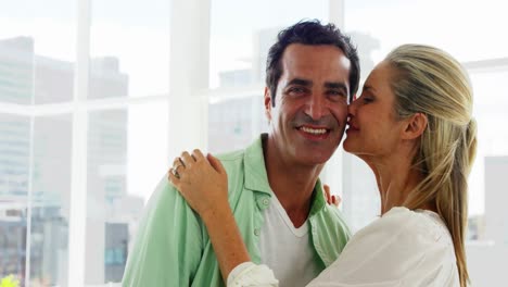 Smiling-woman-kissing-on-mans-cheek-in-living-room-at-home