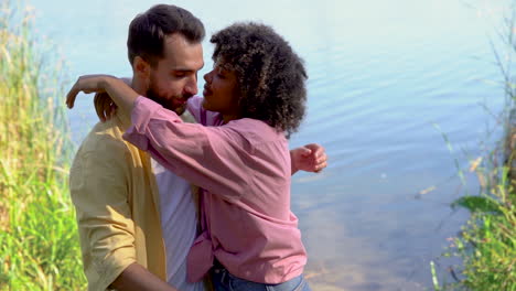 romantic couple hug by a lake in the forest. caucasian man and young black female outdoors.