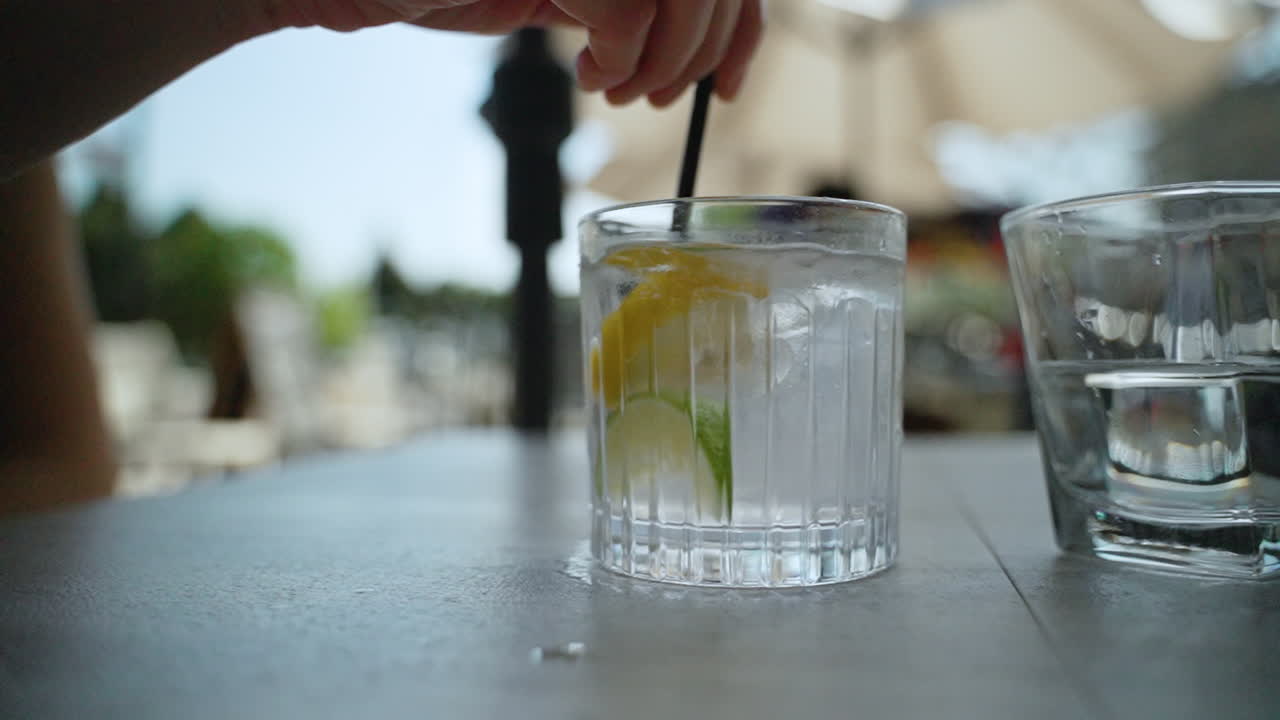 Una mano usa una cannuccia per mescolare un bicchiere d'acqua con cubetti di ghiaccio, limone e lime