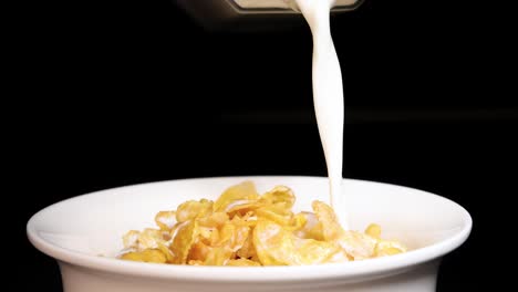 milk cascades into a bowl of crunchy corn cereal against a black background, highlighting texture and motion