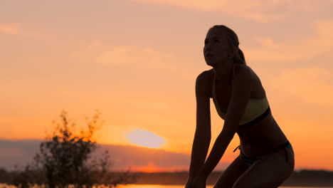 Athletic-girl-playing-beach-volleyball-jumps-in-the-air-and-strikes-the-ball-over-the-net-on-a-beautiful-summer-evening.-Caucasian-woman-score-a-point.