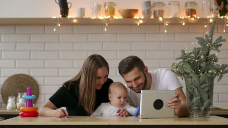 concepto de familia, paternidad y personas - madre y padre felices mostrando una tableta a su bebé en casa