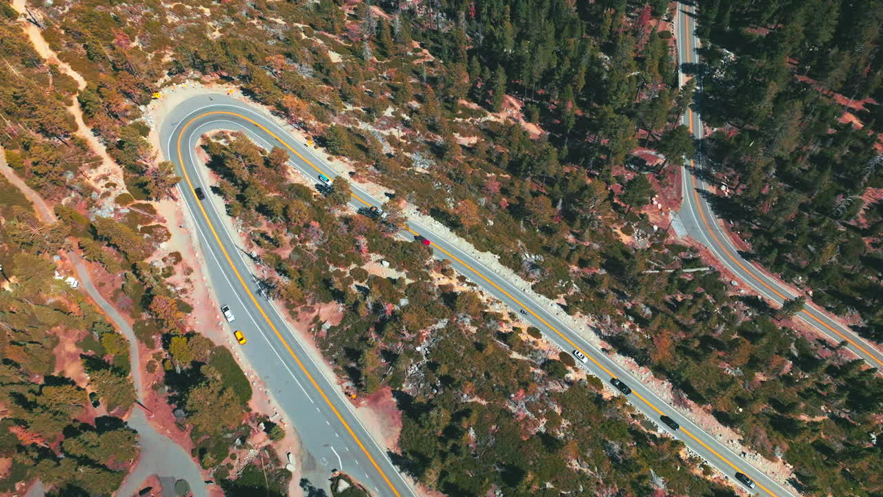 Automobiles slowly moving by the wavy road through the forest. Sunny day footage over the highway at lake Tahoe shore.