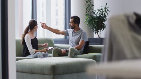 Diverse-male-and-female-business-colleagues-sitting-on-sofa-looking-at-tablet-and-talking