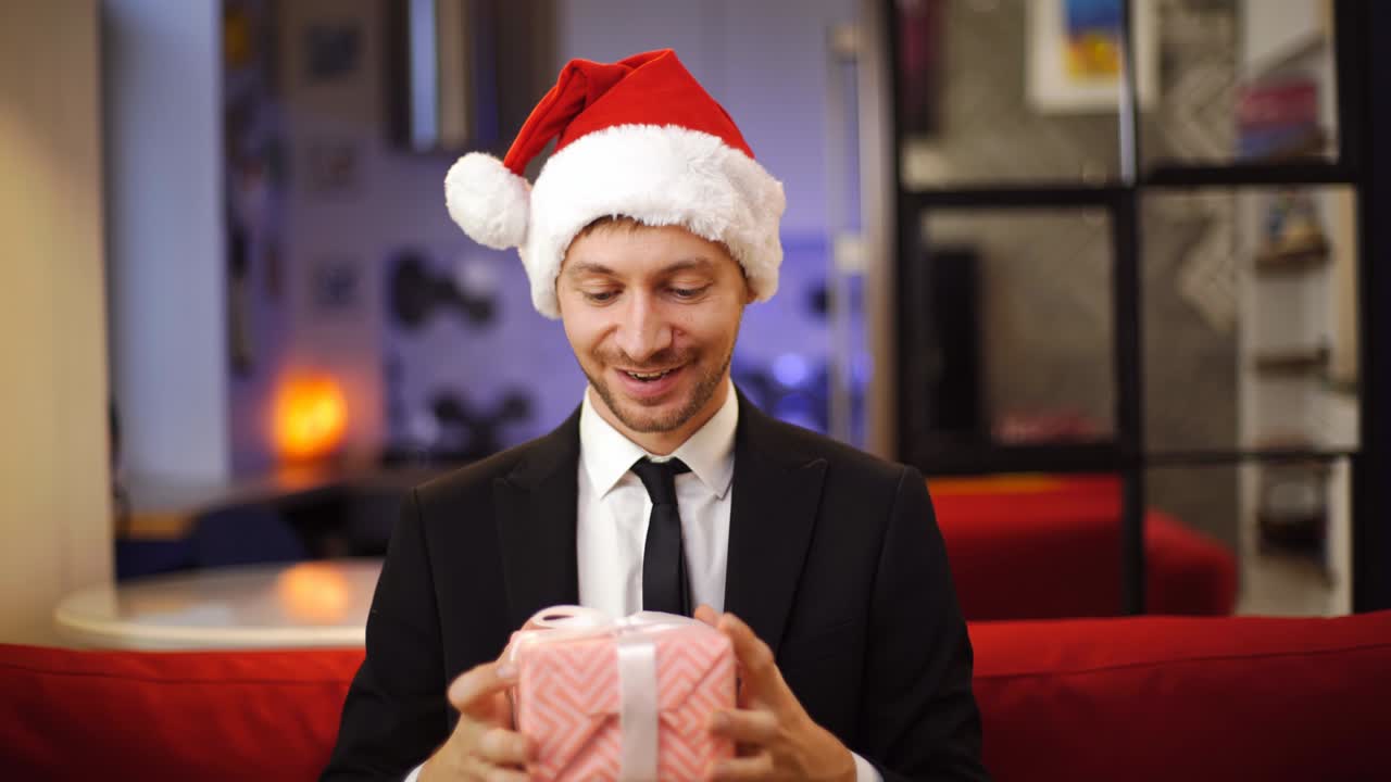 놀란 사업가 빨간 산타 모자를 입고 크리스마스 선물 상자를 들고 있습니다.