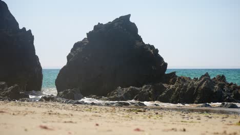 pequeñas olas oceánicas bañando una formación rocosa costera galesa aguda y dentada con montañas nebulosas de snowdonia en el fondo