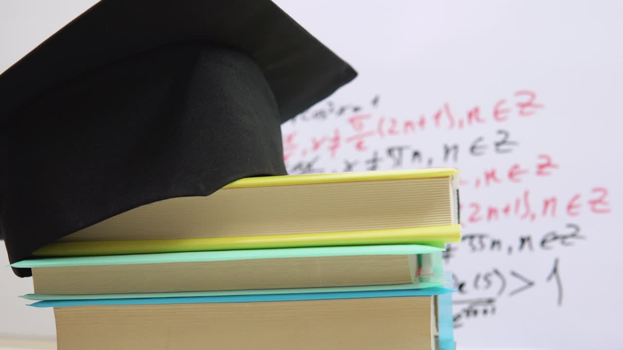 el sombrero cuadrado negro del maestro se encuentra en los libros de texto apilados en una columna. los atributos de un graduado universitario giran alrededor de su eje en un soporte
