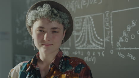 young person in a hat in front of a science chalkboard