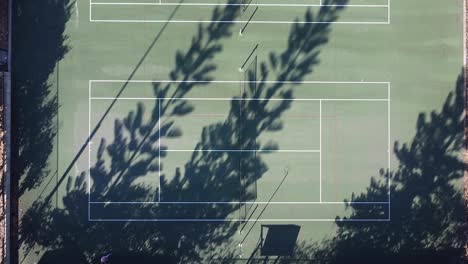 Tennis-Court-Aerial-Rise-Up-View-with-Long-Shadows-Of-Trees