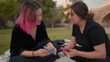 two friends talking and looking at smartphones in a park