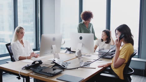 millennial black woman walking around an office talking to her female creative colleagues, lockdown