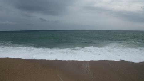Anglet beach with waves breaking on shore, cloudy day, Pyrénées-Atlantiques, France. Aerial drone flying at low altitude over water surface