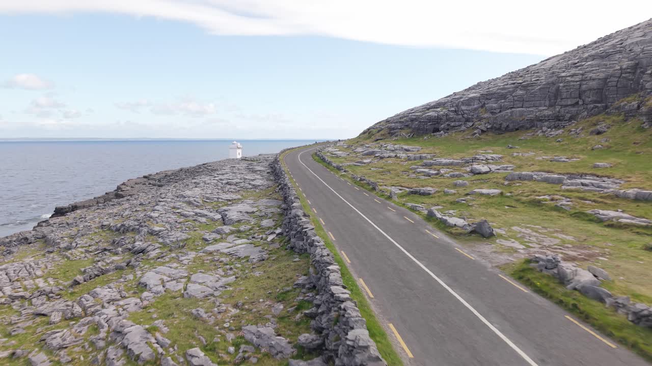 A winding road stretches along rocky coastal terrain, overlooking the calm sea in The Burren, County Clare, Ireland