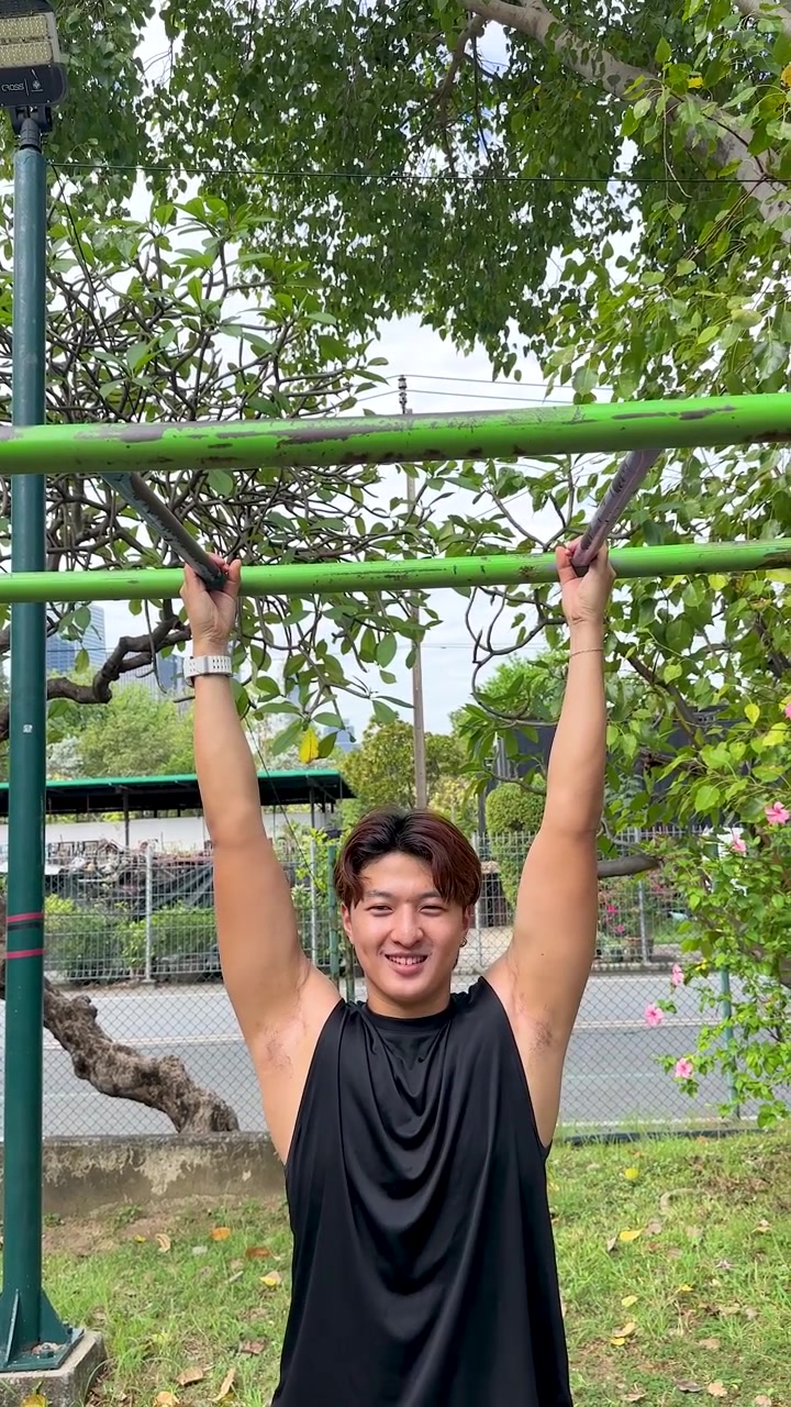 Fit young man in black tank top performs pull-ups at an outdoor gym