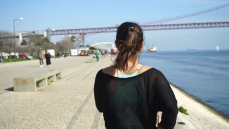 rear view of sporty girl running along embankment