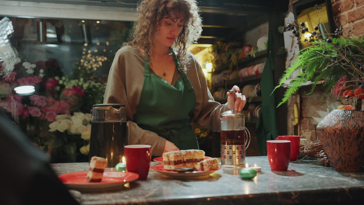 Un barista prepara caffè con french press tra decorazioni floreali e un ambiente accogliente. Elegante esposizione floreale dietro al barista che serve caffè french press appena fatto in un ambiente accogliente.