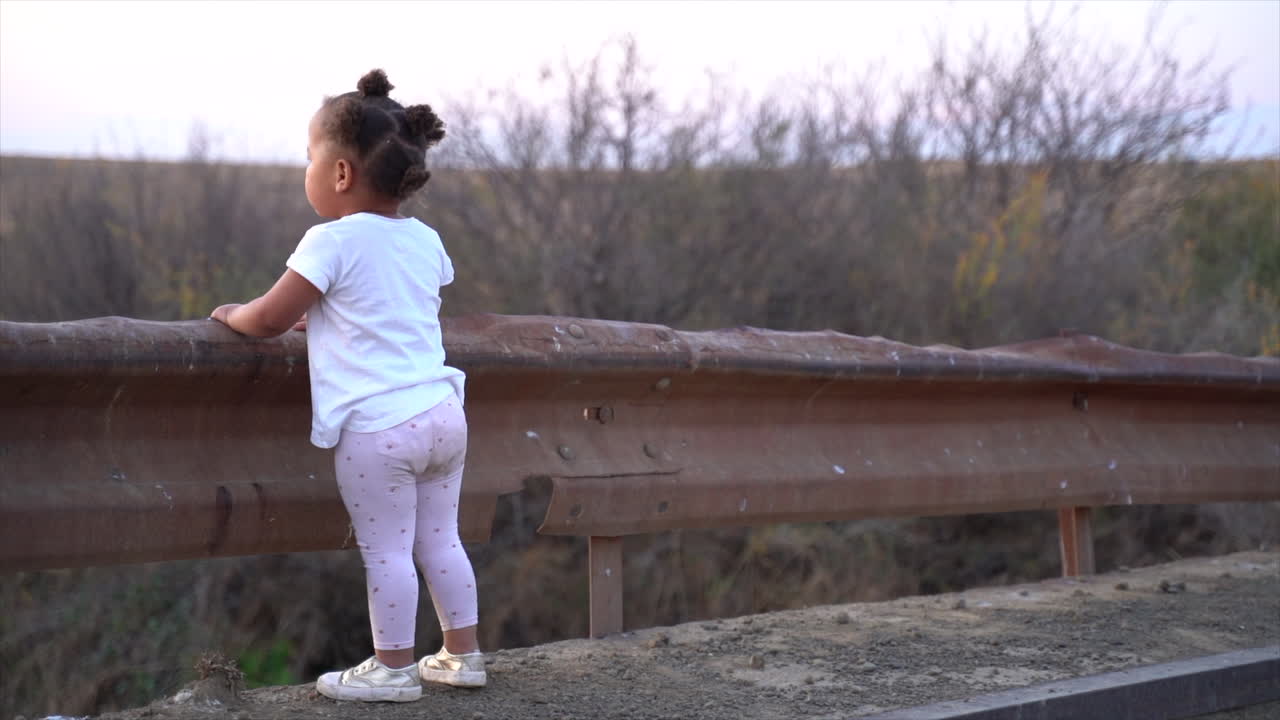 pequeña niña sudafricana parada en un puente bajo en el campo al atardecer en un paisaje invernal y mira a su derecha