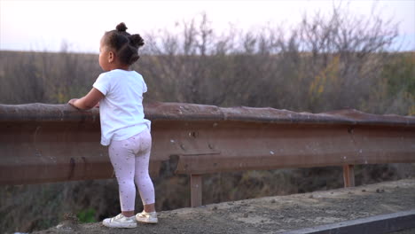 Small-South-African-girl-standing-on-a-low-bridge-in-the-countryside-at-sunset-in-a-winter-landscape-and-looks-to-her-right