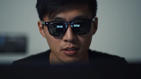 a focused individual wearing sunglasses is deeply engaged with a computer screen, embodying a moment of concentration and technological interaction