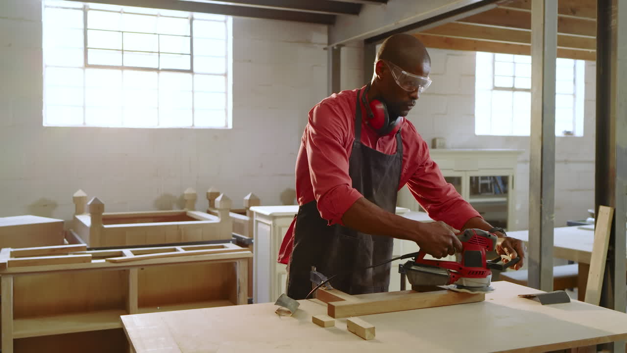 Picking up orbital sander, African American carpenter sanding plank at workshop smoothing surface