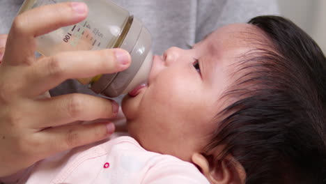 close-up shot of a newborn born child as she is sucking some formula milk from a baby bottle as she is being held in her mother's arms