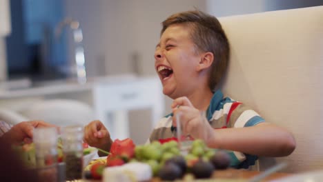 Feliz-Nieto-Caucásico-Riéndose-De-La-Mesa,-Sentado-Al-Lado-Del-Abuelo-Durante-La-Comida-Familiar