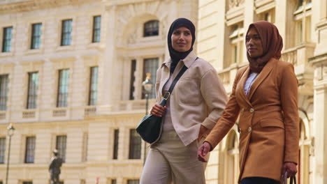 Two-Muslim-Businesswomen-Wearing-Hijabs-With-Modern-Business-Suits-Walking-To-Work-Past-City-Office-Buildings